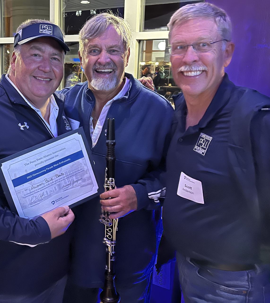 three alumni band members holding certificate and smiling